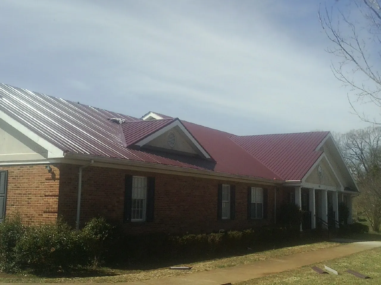Red metal roof with gabled entries on a long brick building, from a Hail Damage Roof Repair job in Johnstown