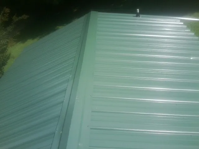 New green metal panels meeting at the ridge of a roof — Flat Roof Repair work by our crew in Johnstown