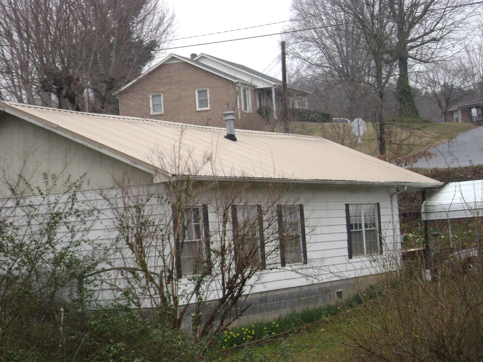 Tan metal roof on a white sided house set into a hillside — Commercial Roofing by Roofing Brothers in Johnstown